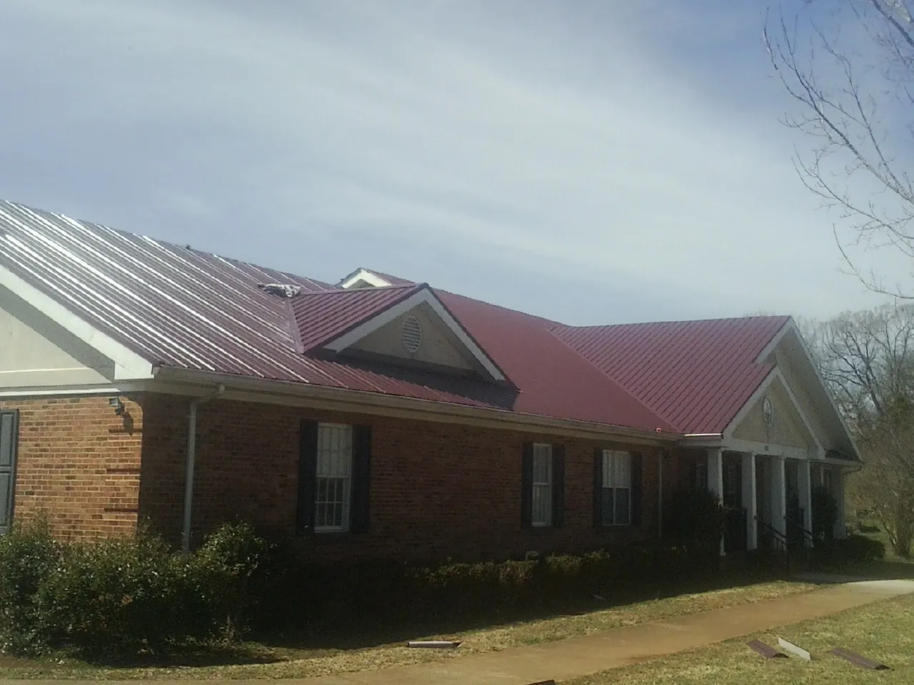 Red metal roof with gabled entries on a long brick building, from a Hail Damage Roof Repair job in Barataria