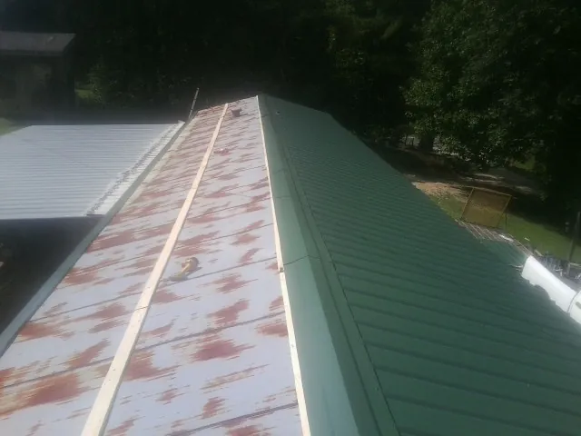 Old rusted panels beside newly installed green metal roofing — Wind Damage Roof Repair by Roofing Brothers in Barataria