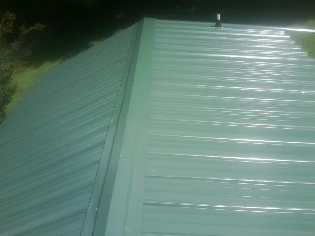 New green metal panels meeting at the ridge of a roof — Flat Roof Repair work by our crew in Barataria