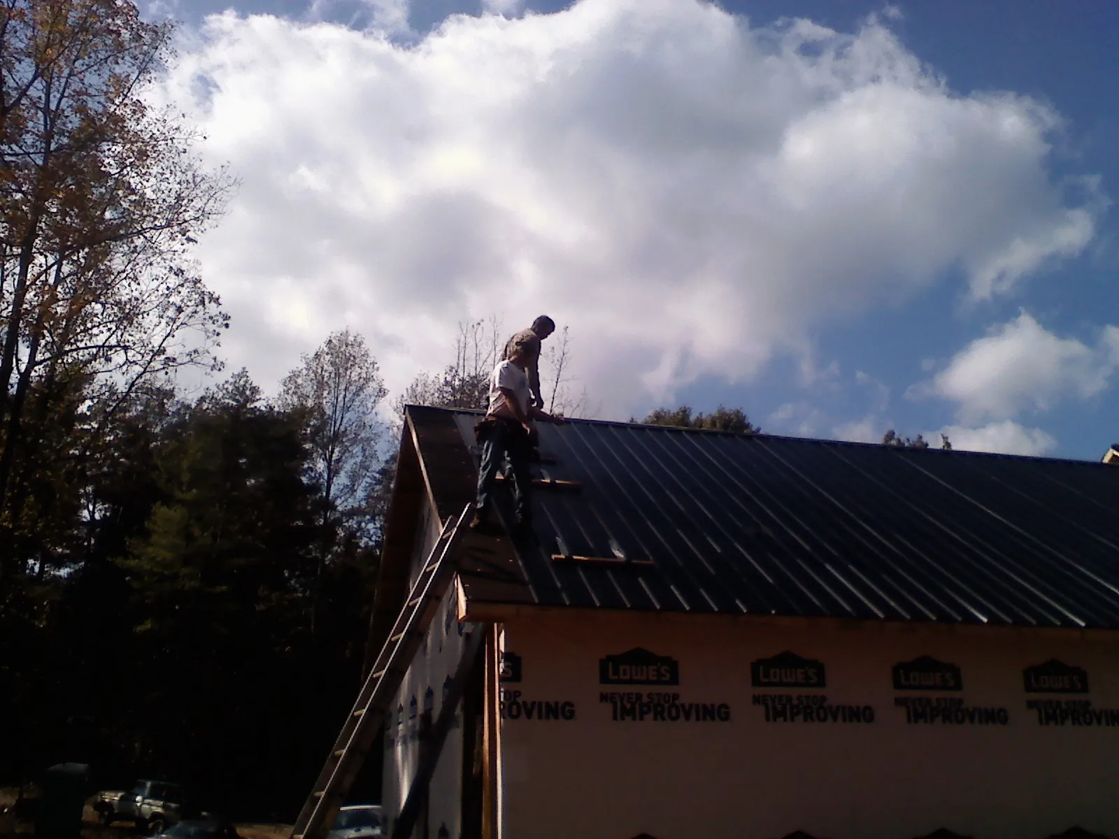 Roofer fastening dark metal panels high against a cloudy sky, from a Roof Inspection job in Barataria