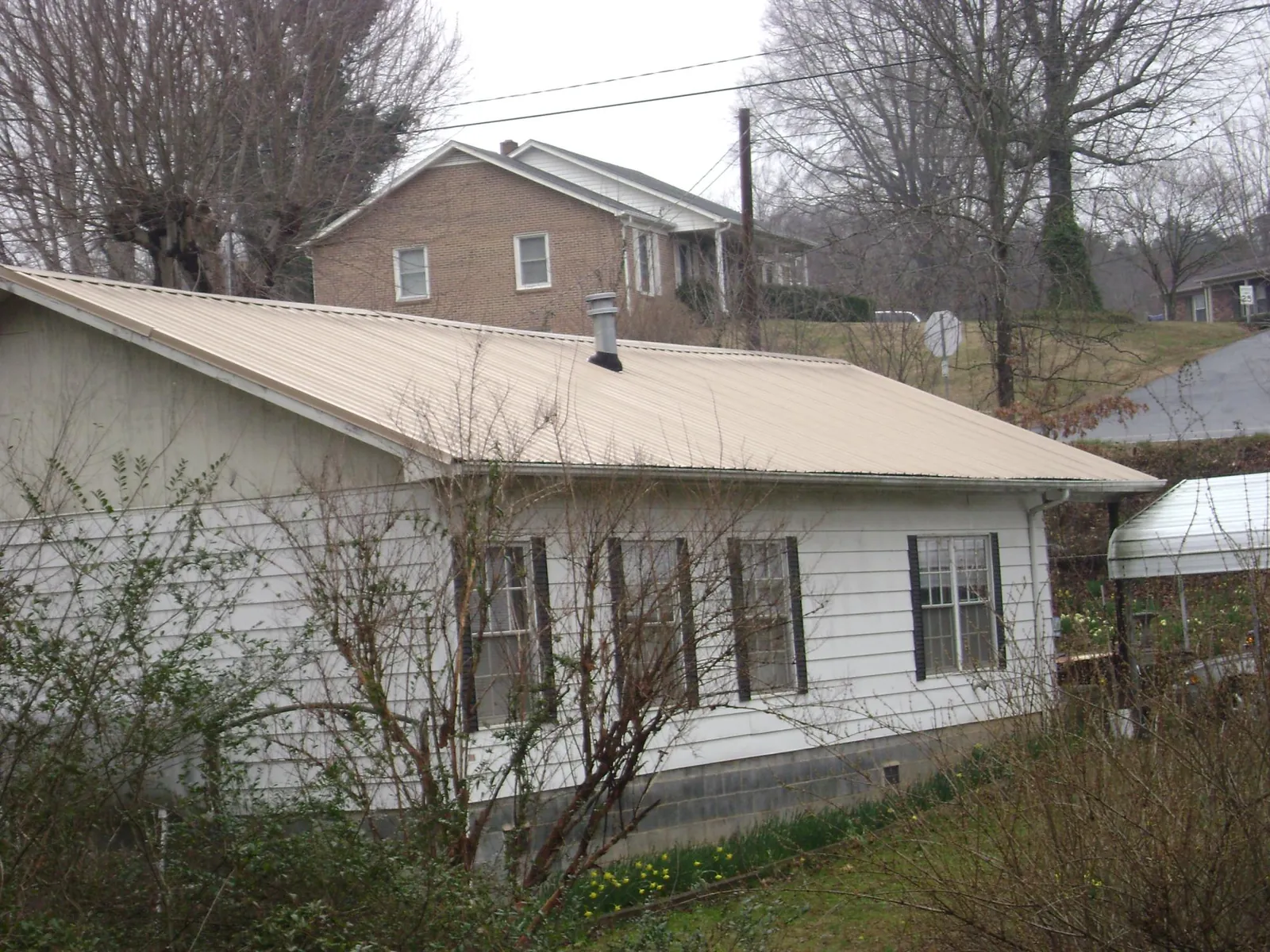 Tan metal roof on a white sided house set into a hillside — Commercial Roofing by Roofing Brothers in Barataria